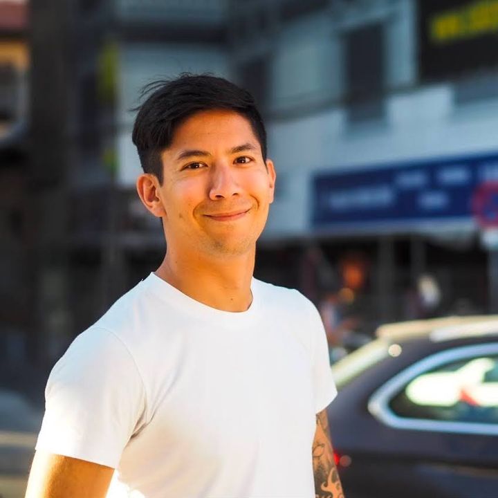 Mahiko Konishi smiling on a sunny street, wearing a white t-shirt
